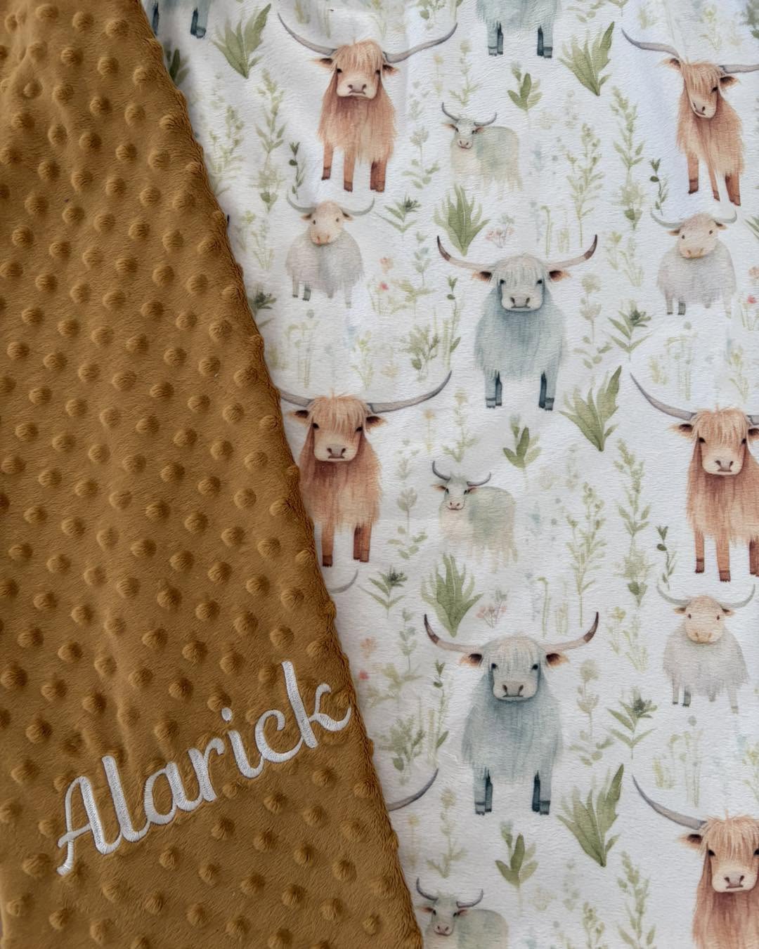 Gros plan d’une couverture : tissu imprimé de vaches highland, Minky moutarde et prénom Alarick brodé